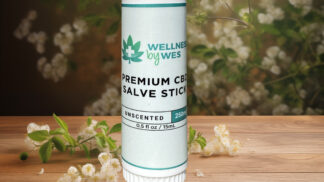 Premium CBD Salve Stick by Wellness by Wes, 250mg, unscented, presented on a wooden surface with white flowers and greenery in the background.